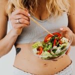 Woman in sports attire enjoys a fresh, nutritious salad, embodying a healthy lifestyle.